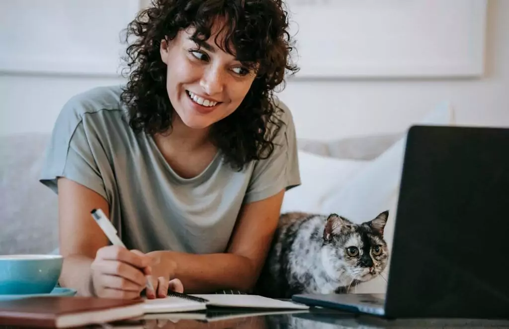 woman with esa cat writing in planner while using laptop