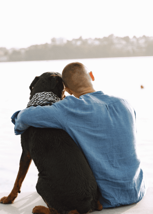 man hugging black dog by lake esa letter wellness wag